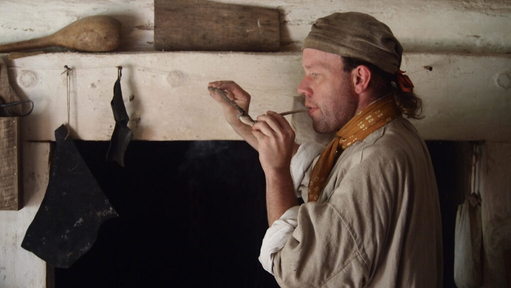 Costumed interpreter lighting a tobacco pipe at Claude Moore Colonial Farm. (2019)